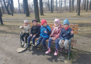 5 dzieci siedzi na ławce przy stawie